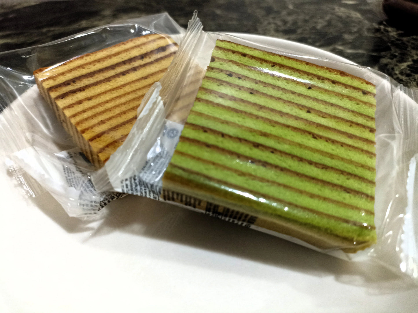 Individually wrapped pandan and original layered cake slices on a plate